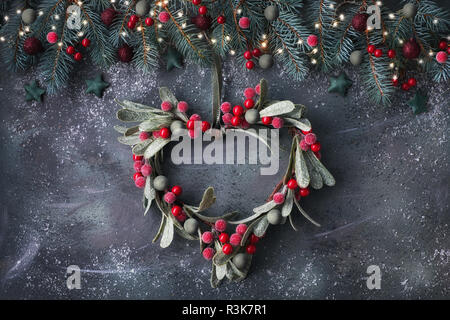 Le gui en forme de coeur couronne de Noël et de fête guirlande faite de brindilles de sapin, baies givrées et bibelots, sur fond sombre Banque D'Images