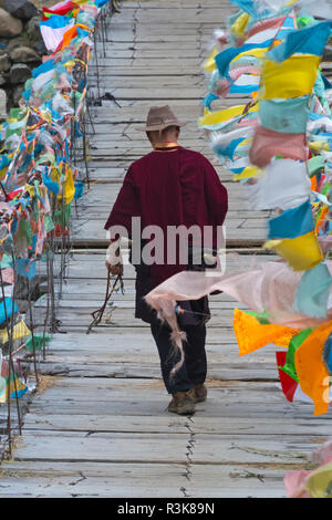 Homme tibétain marche sur pont suspendu décorée de drapeaux de prière, Tagong, l'ouest du Sichuan, Chine Banque D'Images