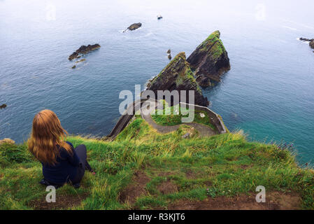 Fille est assise sur une falaise au-dessus de l'océan en Irlande Banque D'Images