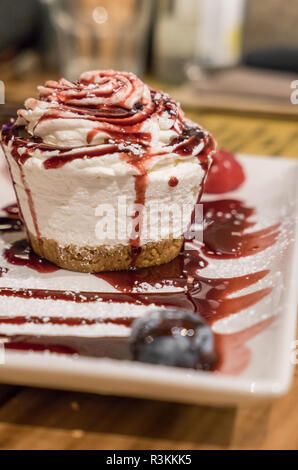 Petite ronde gâteau au fromage avec sauce pour fruits des bois, avec une pincée de sucre en poudre. Banque D'Images