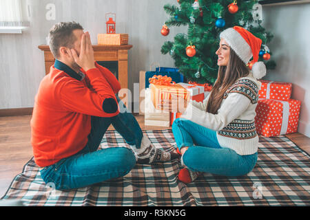 Photo de l'homme assis en face de femme et garde les yeux fermés. Elle est titulaire d'présente pour lui. Jeune femme a l'air confiant et joyeux Banque D'Images