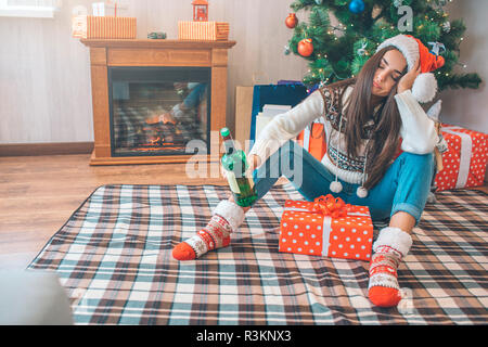 Jeune femme assise sur le plancher et dort. Elle est titulaire d'vert bouteille d'alcool dans la main. Il y a une boîte avec présente entre ses jambes. Elle est ivre Banque D'Images