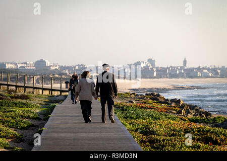 Senior couple promenade le long de la promenade près de l'océan. Les personnes éloignées. Cityscape background. Vue arrière. Copier l'espace. Banque D'Images