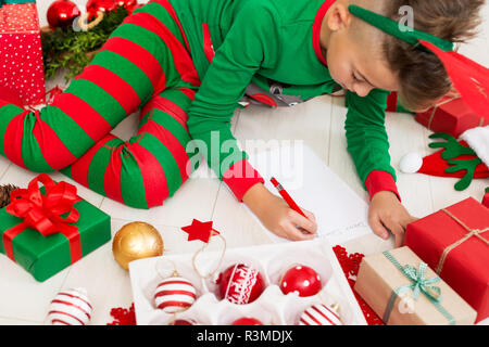 Cute boy wearing christmas pyjama écrit lettre au Père sur salon-de-chaussée. Vue aérienne d'un jeune garçon écrit ses cadeaux de Noël. Banque D'Images