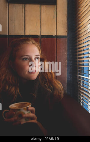 Femme rousse à la fenêtre grâce à blind in cafe Banque D'Images
