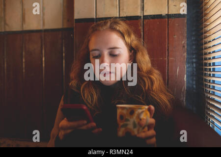 Woman using mobile phone while having coffee in cafe Banque D'Images