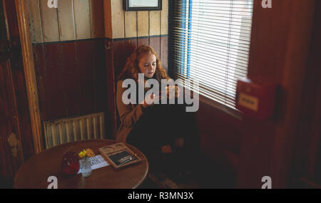 Woman using mobile phone while having coffee in cafe Banque D'Images