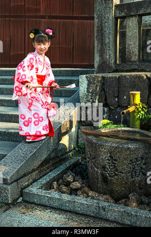 Kyoto, Japon. Jeune fille vêtue d'un kimono, utilise une louche (hishaku traditionnel) à boire à partir d'un bien commun au printemps le Temple Kiyomizu-dera Banque D'Images