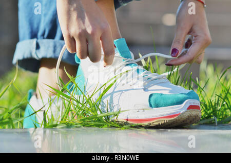 Jeune fille portant des jeans attacher ses lacets de sneakers debout sur l'herbe verte side view close-up photo horizontale, journée ensoleillée Banque D'Images