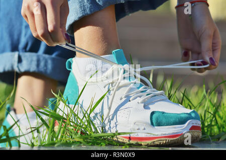 Jeune fille portant des jeans attacher ses lacets de sneakers debout sur l'herbe verte side view close-up photo horizontale, journée ensoleillée Banque D'Images