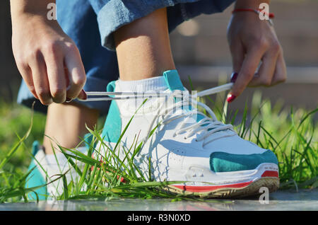 Jeune fille portant des jeans attacher ses lacets de sneakers debout sur l'herbe verte side view close-up photo horizontale, journée ensoleillée Banque D'Images