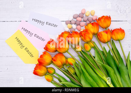 Un bouquet de tulipes avec les oeufs de pâques sur un fond en bois avec un heureux message de Pâques Banque D'Images