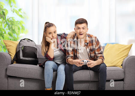 Ennuyer adolescente assise à côté d'un garçon à jouer à des jeux vidéo sur un canapé à l'intérieur Banque D'Images