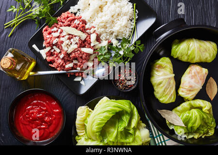 Feuilles de chou farcies non cuites avec des ingrédients - la viande hachée, le riz cuit, le persil et la sauce tomate sur un tableau noir, vue de dessus, flatlay Banque D'Images