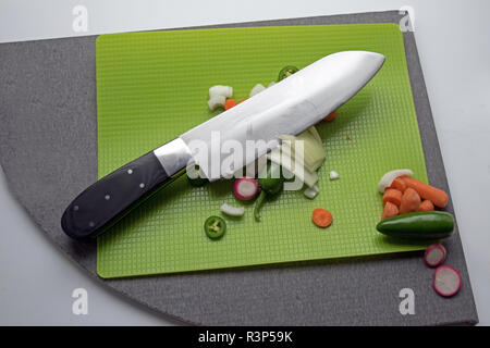 Un grand couteau est utilisé pour couper des légumes sur un tapis vert. Banque D'Images