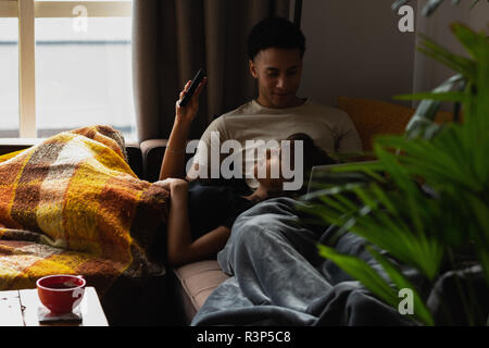 Couple using mobile phone on sofa in living room Banque D'Images