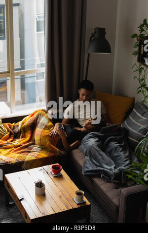 Couple relaxing on sofa in living room Banque D'Images