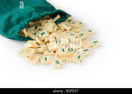 Jeu de Scrabble aléatoire lettre carreaux avec valeur score sortant de leur sac de cordon vert, isolé sur fond blanc. Banque D'Images