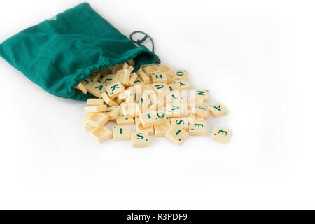 Jeu de Scrabble aléatoire lettre carreaux avec valeur score sortant de leur sac de cordon vert, isolé sur fond blanc. Banque D'Images