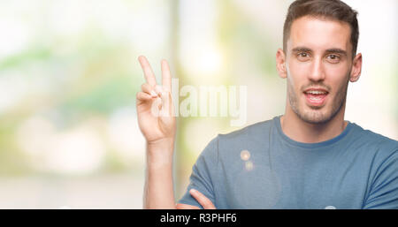 Beau jeune homme souriant avec happy face à l'appareil photo faisant un clin la victoire. Numéro deux. Banque D'Images