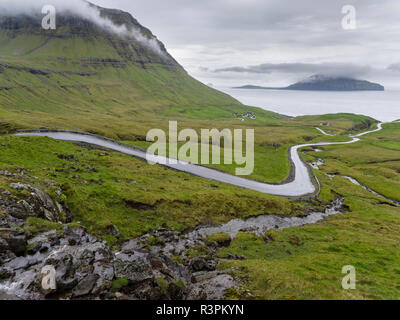 Route de montagne à l'Nordradalur à la côte ouest. L'île de Koltur en arrière-plan. Le Danemark, Îles Féroé Banque D'Images