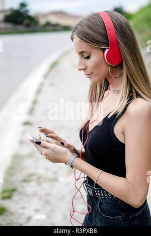 Teenage girl du riverside wearing headphones using cell phone Banque D'Images