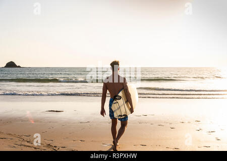 Jeune homme marchant sur la plage, sa planche de surf Banque D'Images