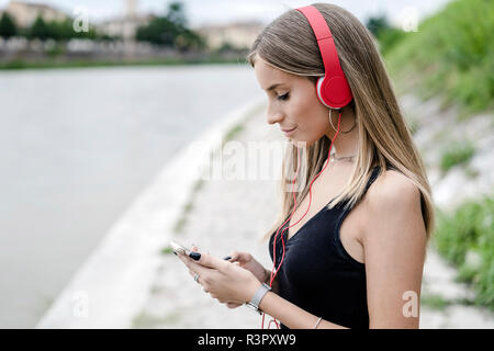 Teenage girl du riverside wearing headphones using cell phone Banque D'Images