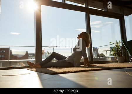 Relaxed mature woman sitting on tapis dans la lumière du soleil à la maison Banque D'Images