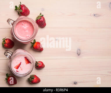 Les smoothies rouge fait des fraises et du lait, dans un élégant pot, une rangée de baies sont exposées, sur un fond de bois blanc, une frontière, une place pour le texte Banque D'Images