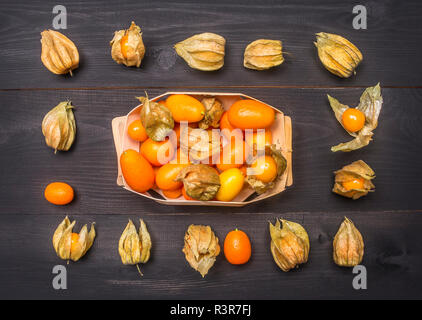 Les physalis, disposés autour d'un panier sur un fond rustique noir, vue du dessus des aliments sains, les fruits exotiques Banque D'Images