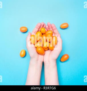 Girl holding une poignée de kumquat mûrs sur un fond lumineux bleu, vue du dessus Banque D'Images