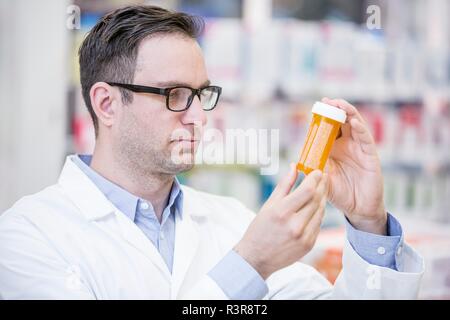 Pharmacien mâle lecture étiquette sur bouteille de pilules en pharmacie. Banque D'Images