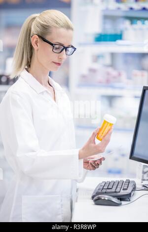 Female pharmacist reading étiquette sur bouteille de pilules en pharmacie. Banque D'Images