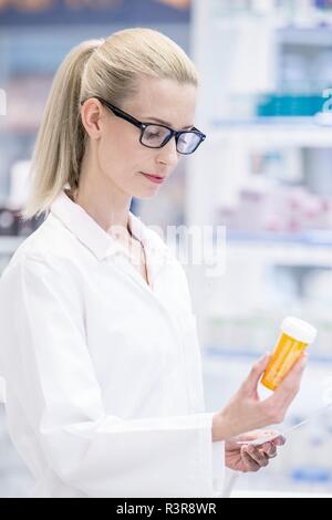 Female pharmacist reading étiquette sur bouteille de pilules en pharmacie. Banque D'Images