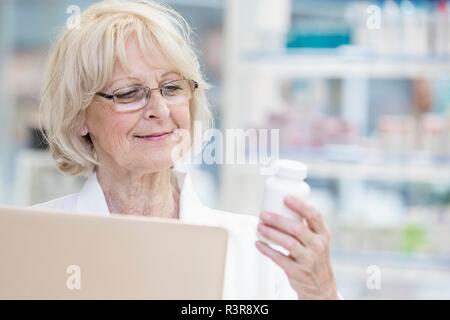 Hauts female pharmacist holding laptop et la lecture de l'étiquette sur bouteille de pilules en pharmacie. Banque D'Images