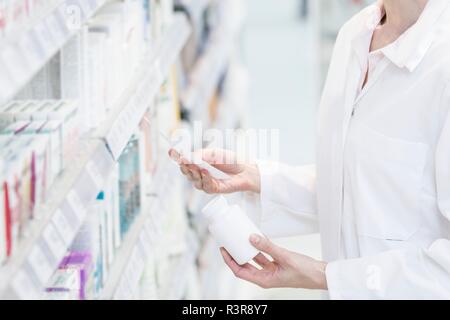 Female pharmacist reading prescription avec bouteille de pilules dans une main en pharmacie. Banque D'Images