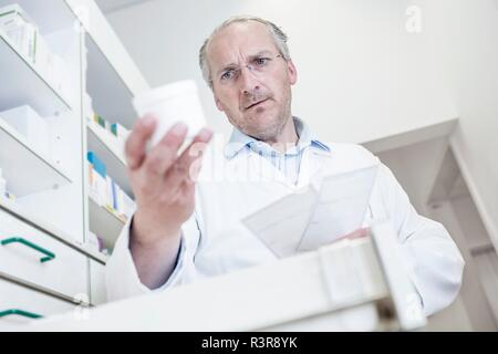 Pharmacien mâle lecture étiquette sur bouteille de pilules alors qu'à la médecine en tiroirs en pharmacie. Banque D'Images