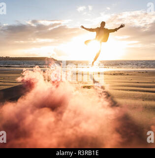 Homme formation mouvement à la plage avec la fumée colorée au coucher du soleil Banque D'Images