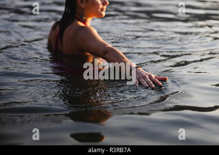 Main de jeune femme de toucher la surface de l'eau dans un lac Banque D'Images