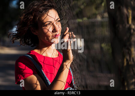 Portrait de jeune femme en ombre de Wire Mesh fence sur son visage à la recherche à distance Banque D'Images