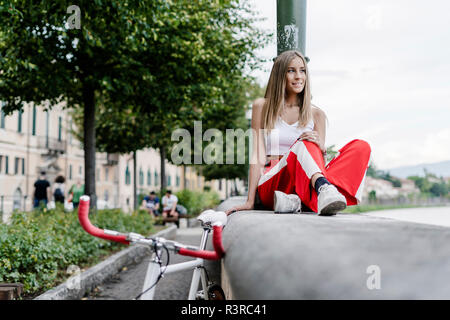 Smiling teenage girl assis sur un mur à côté de la rivière location Banque D'Images