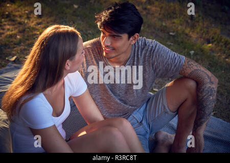 Couple assis dans un parc, profitant de coucher du soleil Banque D'Images