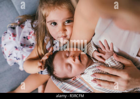 Mother holding her baby close avec sœur se sentir ses cheveux Banque D'Images