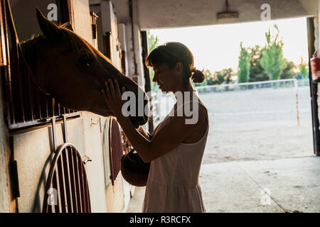 Femme cheval caressant dans stable Banque D'Images