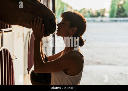 Smiling woman stroking horse stable en Banque D'Images