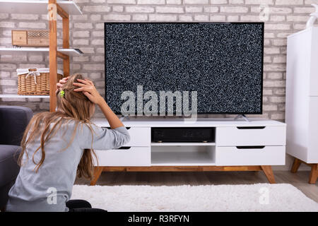 Vue arrière d'une fille frustrée assis près de la télévision avec plus de signal Banque D'Images