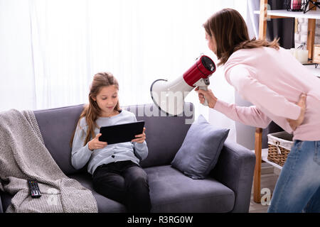 Mère crier par mégaphone à Careless Girl Sitting on Sofa Using Digital Tablet Banque D'Images