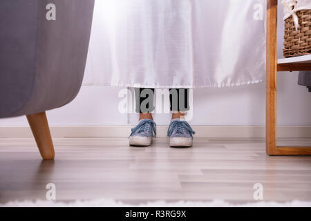 La section basse d'un Girl's pieds derrière le rideau sur plancher de bois franc Banque D'Images