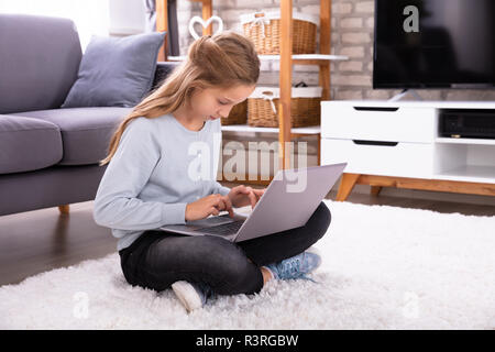 Fille assise sur le tapis à l'aide d'ordinateur portable à la maison Banque D'Images